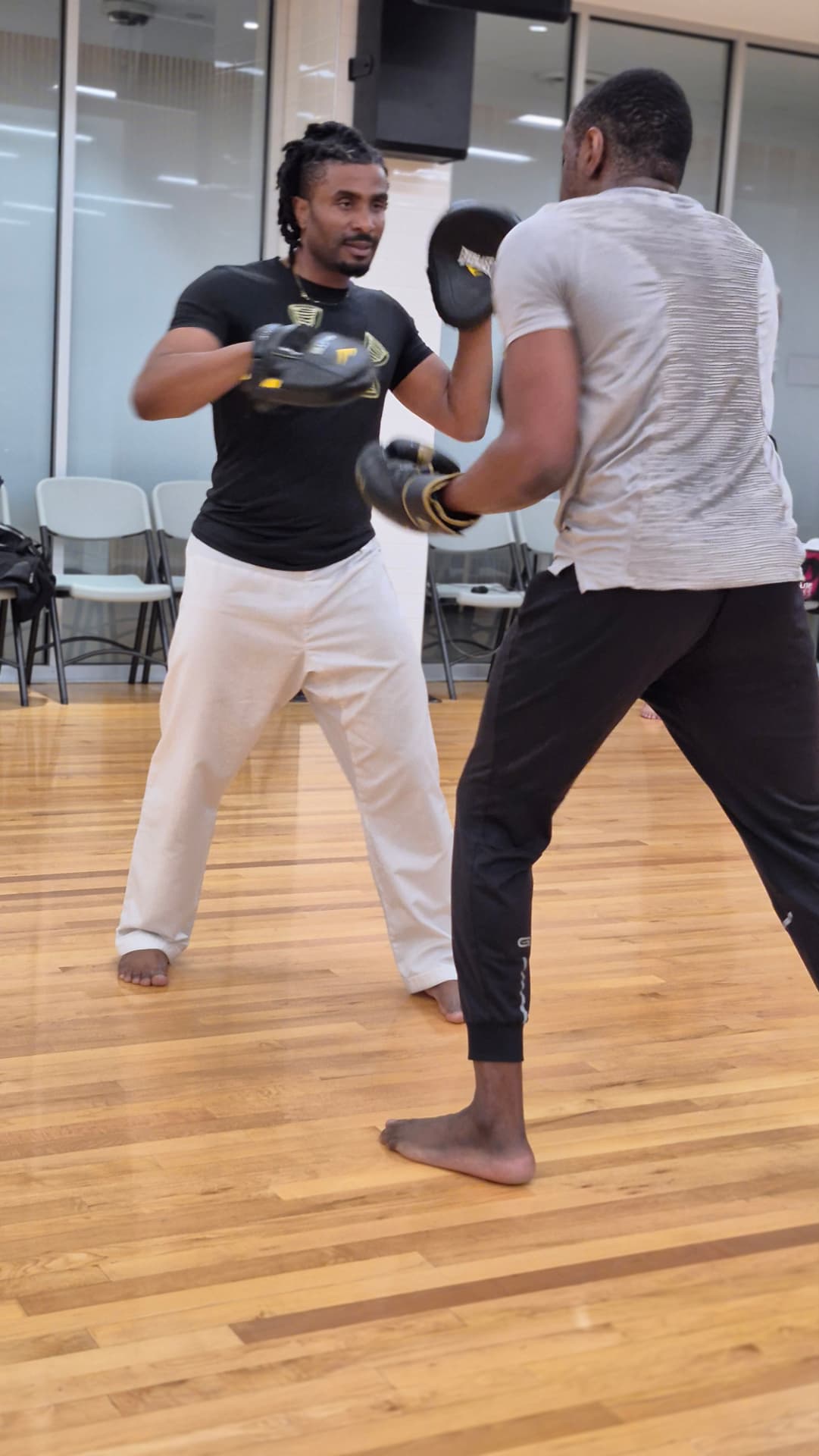 The instructor holds focus mitts as an adult student sets up a combination
