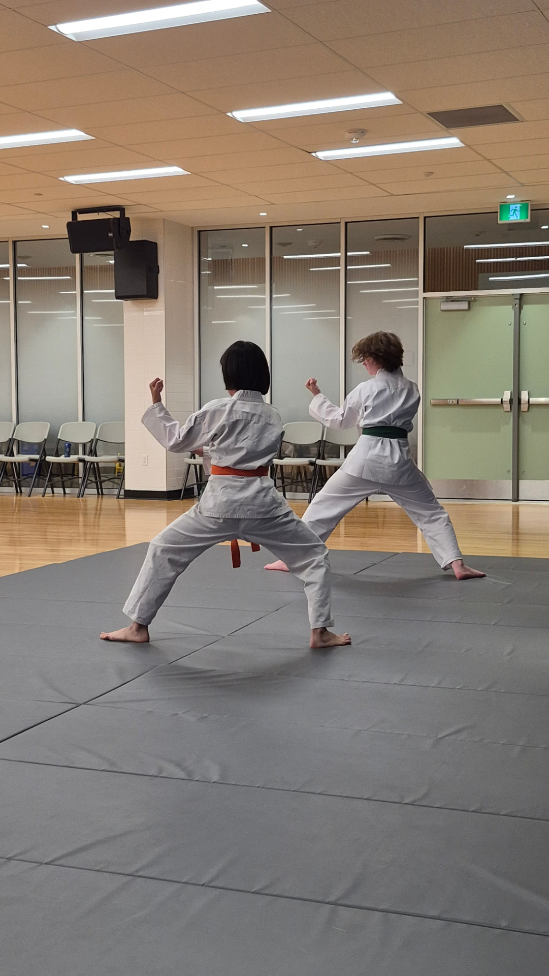 Two children in white karate gi practise partner techniques on grey mats