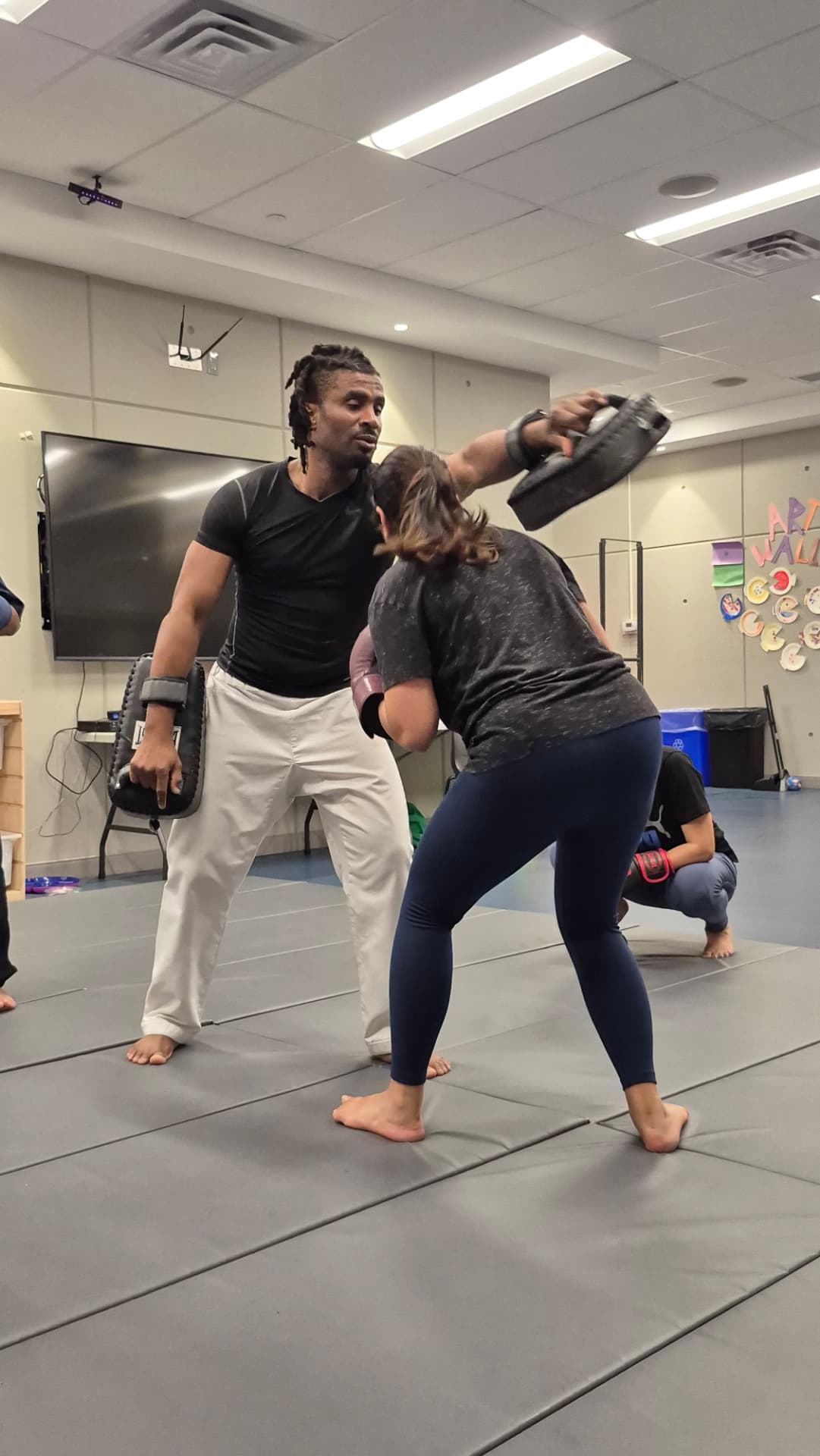 An adult student in gloves works a punching combination on focus mitts