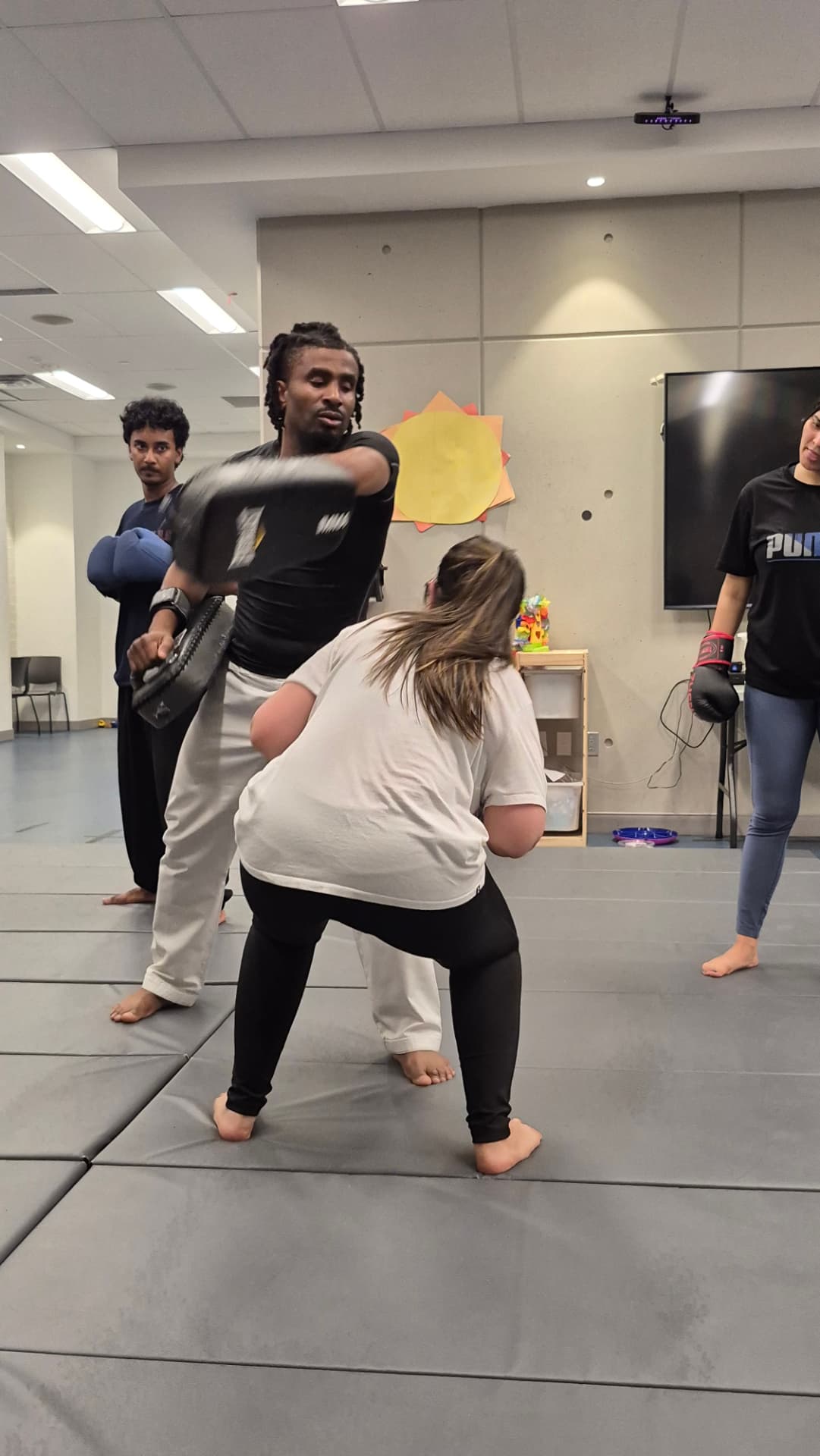 An adult student throws a high roundhouse kick onto a held pad