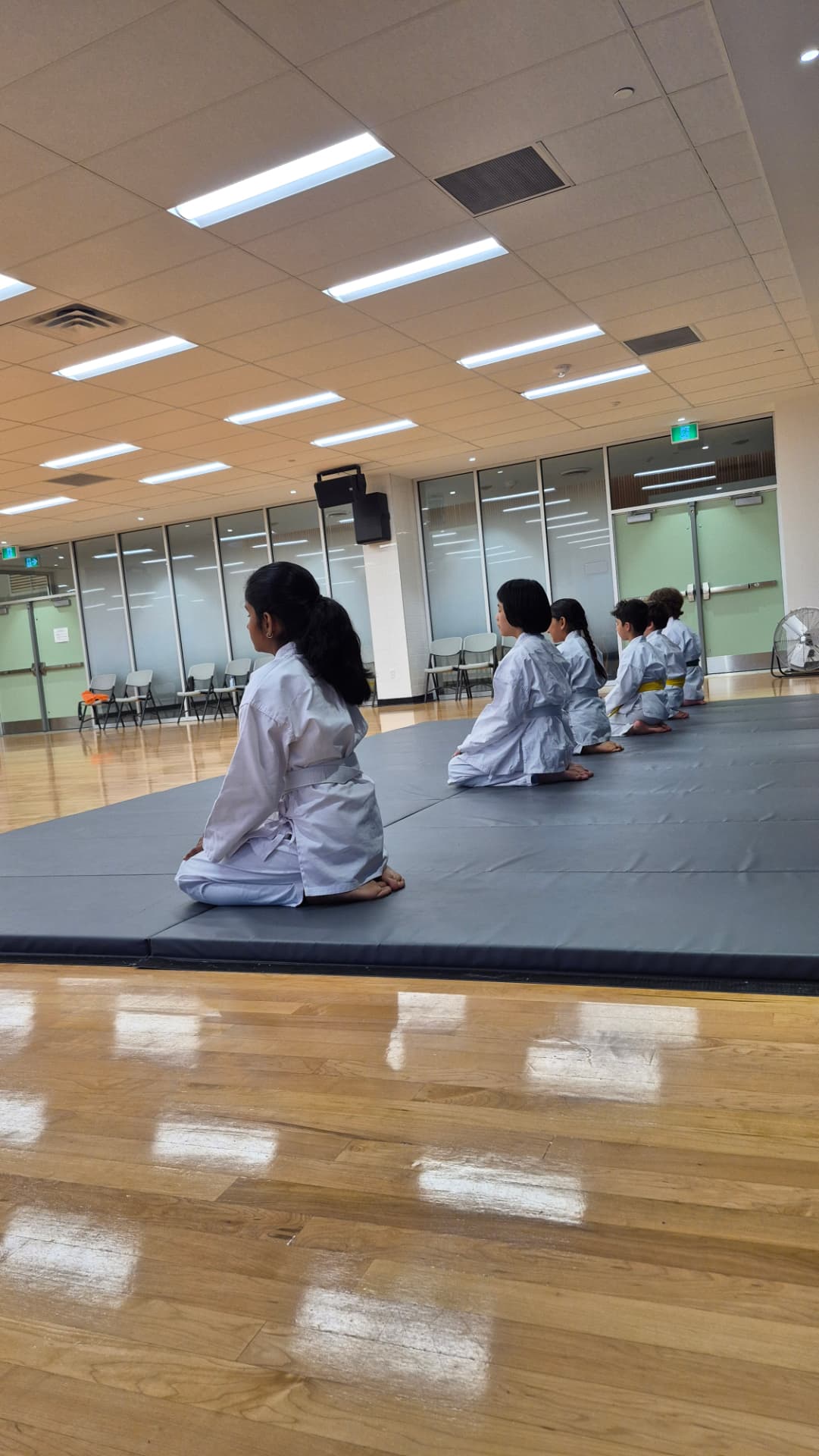 Young karate students sit in an orderly line on the training mats